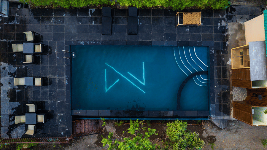 Aerial top-down view of a luxury swimming pool with glowing blue lights and poolside seating at Maati Resort By The Lake Hill, Jeolikote.