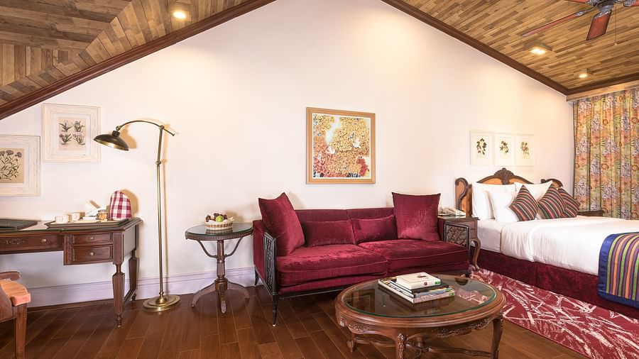 a bed kept beside a maroon sofa - Mayfair Himalayan Spa Resort Kalimpong