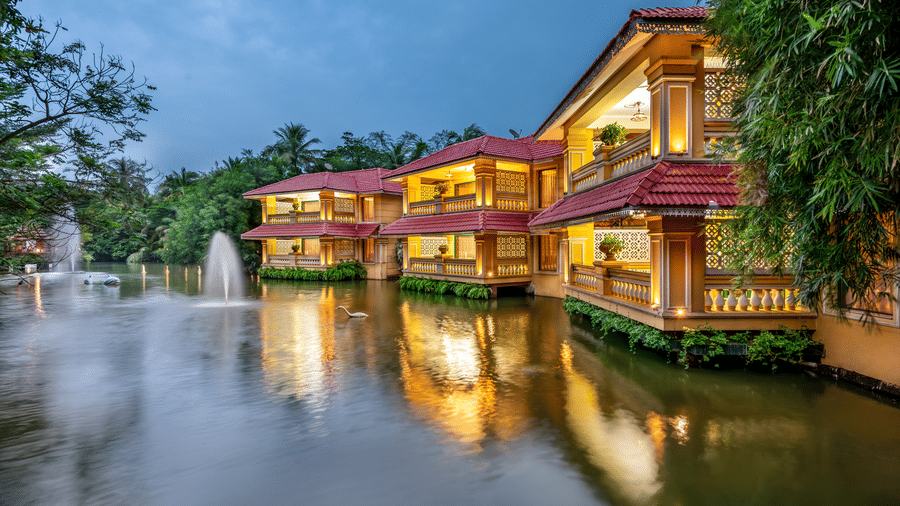 Luxury resort facade of MAYFAIR Lagoon Bhubaneswar illuminated at dusk reflecting on the lagoon with a fountain and swan