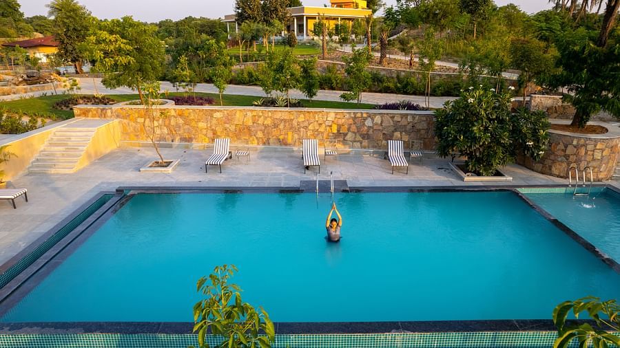 A graceful image of a woman performing an asan in the pool, with a sun lounger on the deck adding to the tranquil vibe - Rajbagh Wellness, Udaipur