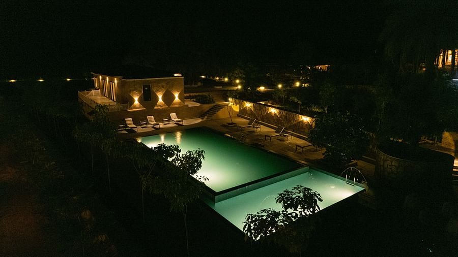 An enchanting aerial view of the swimming pool glowing under blue lights at night, nestled amidst verdant trees - Rajbagh Wellness, Udaipur