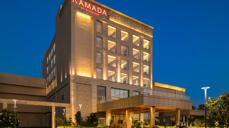 Illuminated facade of Ramada by Wyndham Sonipat Murthal at night featuring modern architecture and a grand entrance.