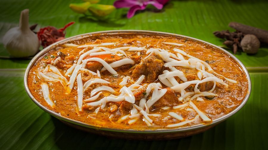  Creamy butter chicken garnished with fresh cream served in a brass dish on a banana leaf, embodying rich Indian flavors - The President Hotel Jayanagar, Bangalore
