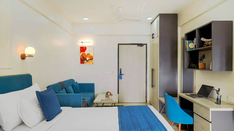 A hotel room at Urban Suites by BluSalzz, Jaipur, featuring with a bed, a desk area with a chair, and a small couch visible.