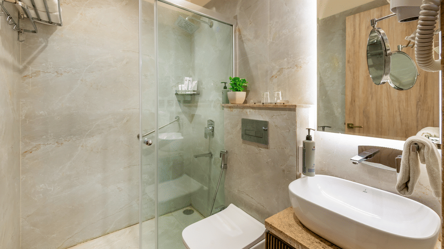 Sleek bathroom at Lords Inn Sangam, Bhopal featuring a glass shower cubicle, white toilet, oval sink, and elegant marble finishes.