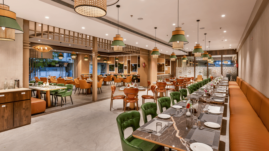 Full view of the Blue Coriander restaurant showcasing emerald green and mustard yellow chairs and tables along with woven pendant lights hanging from ceiling – Skkylight Lords Inn, Nanded