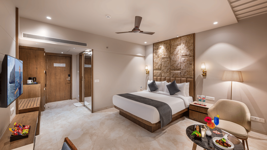 A brightly lit Deluxe Room with a king size bed, elegant wooden panelling, and a modern seating area by the window – Skkylight Lords Inn, Nanded