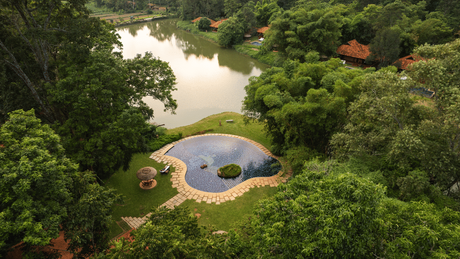 Bird's eye view of Evolve Back Coorg resort with a natural lake surrounded by forest