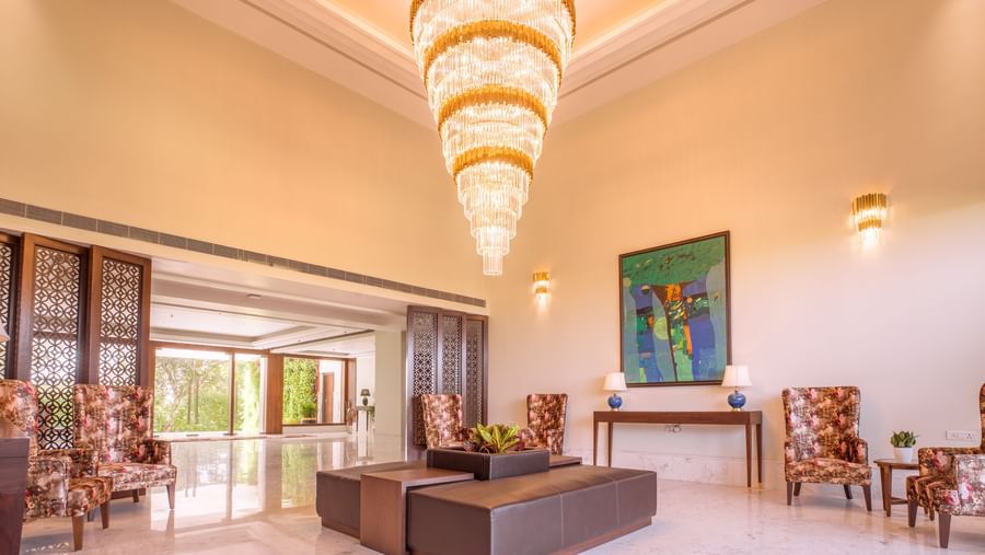 Elegant lobby of The Lalita Grand Mathura - Vrindavan with a grand chandelier, modern seating, floral chairs, abstract art, and marble flooring.