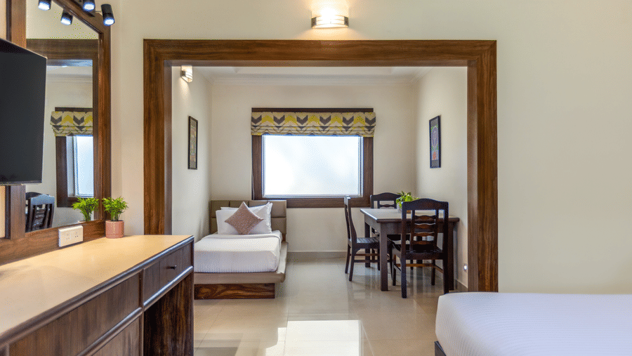 A hotel room with a single bed and a dining table, seen through a wooden doorway - Mango Hill Resort, Coimbatore