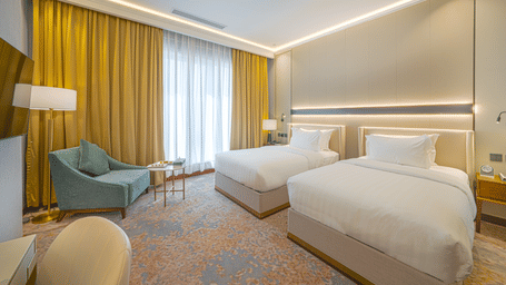 Twin Beds in a Standard Room at Grand Iva Hotel, Abha, showcasing the plush beds, closed curtains, bedside tables, contemporary interiors, and bright lighting.