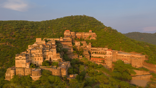 Neemrana Fort Palace surrounded by lush greenery and green hills. The property is huge and spread across the land with several sections.