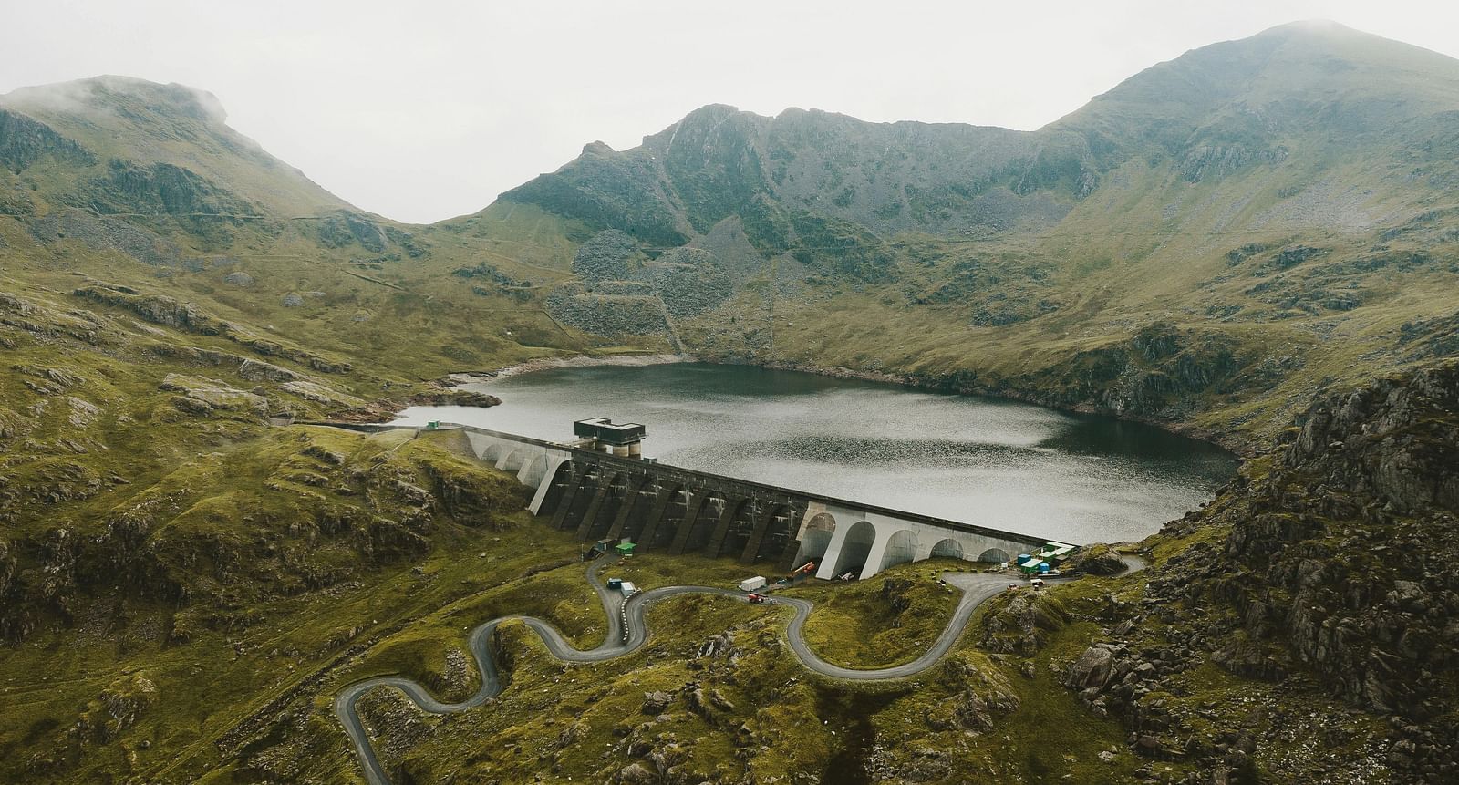 image of a dam holding water situated in the middle of greenery and hilly mountain tops