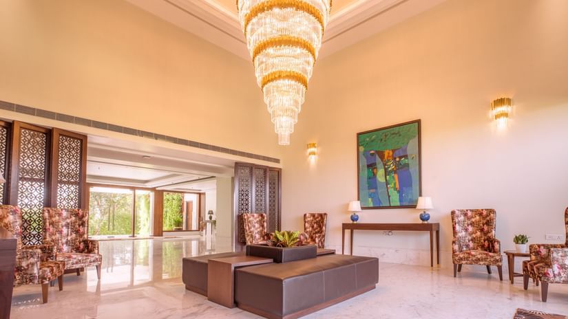 Elegant lobby of The Lalita Grand Mathura - Vrindavan with a grand chandelier, modern seating, floral chairs, abstract art, and marble flooring.