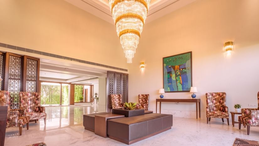 Elegant lobby of The Lalita Grand Mathura - Vrindavan with a grand chandelier, modern seating, floral chairs, abstract art, and marble flooring.