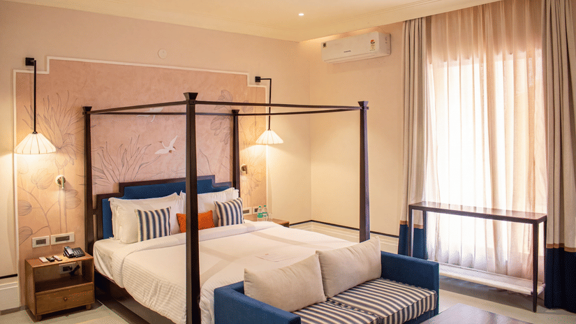 Another view of a bedroom with a four poster king size bed, attached sofa, bedside table, lamp, and curtains at The Sierra - By The Lake.