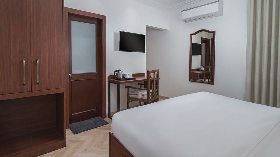 A room with a spacious bed, a wooden wardrobe, a wall-mounted television, and a wooden table directly below it | Hotel Ganga Maiya