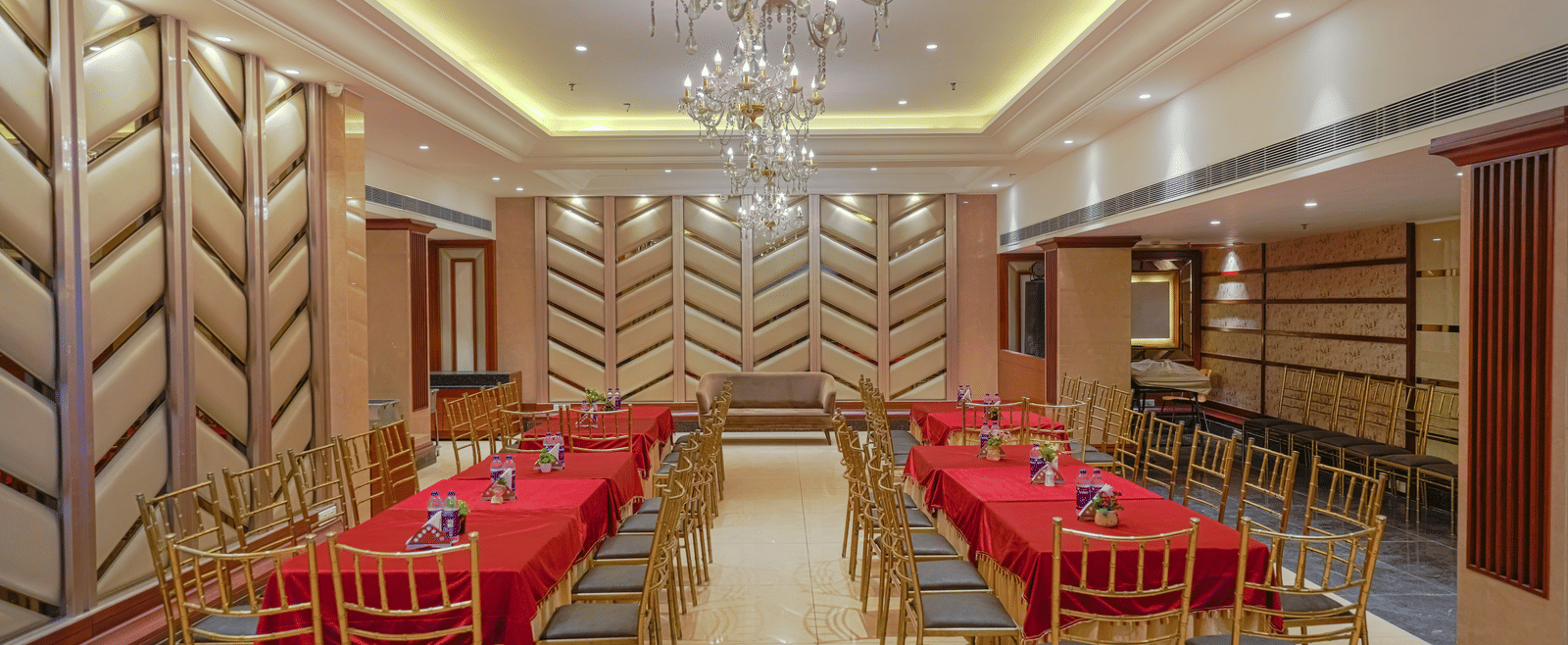 A wide view of the elegant private dining room, set up with multiple rectangular tables and an ornate chandelier at BluSalzz Select City Centre, Amritsar.