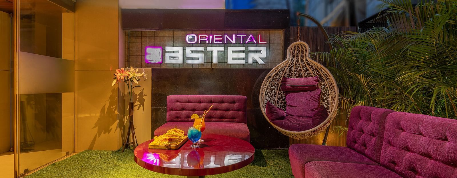 View of the lobby area at Oriental Aster, Mumbai, featuring cushioned sofas arranged around a table and a signboard displaying 'Oriental Aster'.