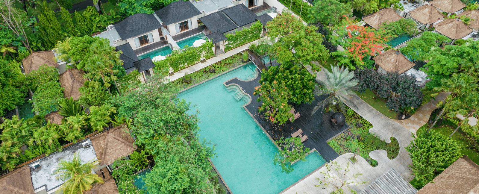 Overhead view of a hotel with a large, tree-lined pool area.