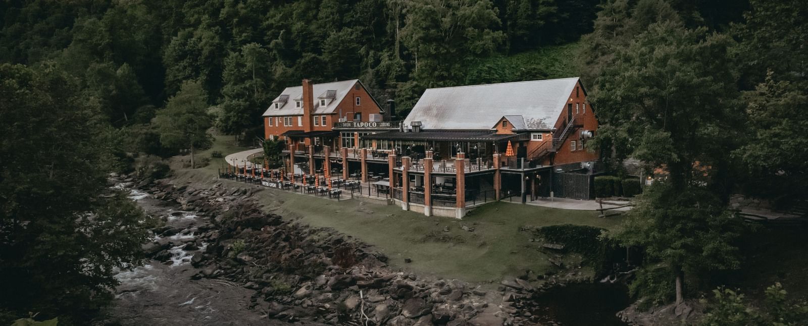 Cottages at the Historic Tapoco Lodge set amidst the tall trees, steep hills, and a stream is running in front of the property.