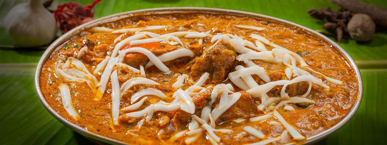  Creamy butter chicken garnished with fresh cream served in a brass dish on a banana leaf, embodying rich Indian flavors - The President Hotel Jayanagar, Bangalore