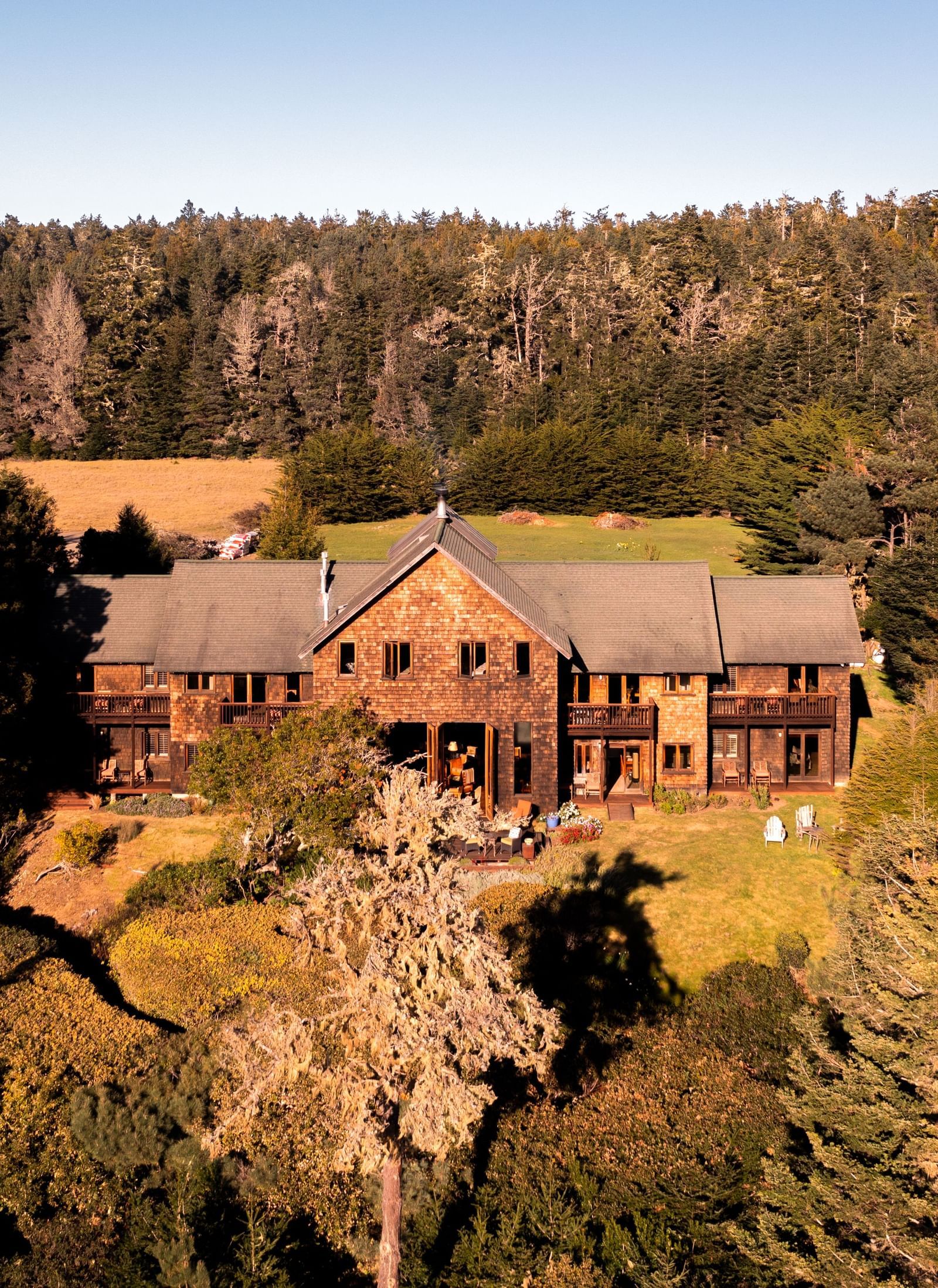 A bright exterior shot of Brewery Gulch Inn, surrounded by lush green trees and gardens with a clear blue sky in the background.