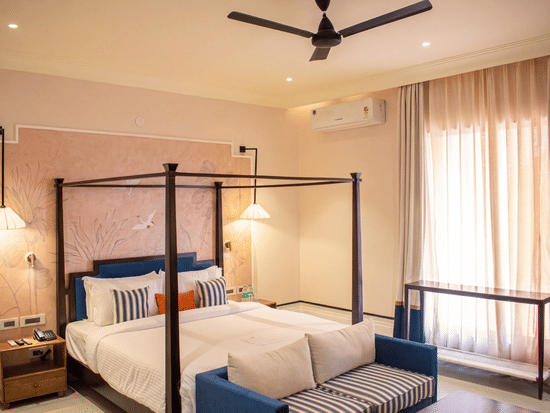 Another view of a bedroom with a four poster king size bed, attached sofa, bedside table, lamp, and curtains at The Sierra - By The Lake.