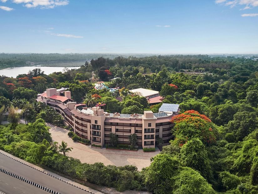 DGV Resort by Treat, Silvassa nestled in dense greenery, featuring a curved main building, waterpark, and nearby river under a clear blue sky.