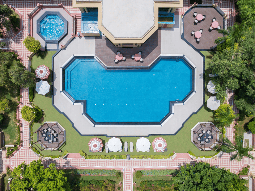 An aerial view of the expansive outdoor swimming pool with a nicely manicured garden surrounding it at the Heritage Village Resorts & Spa, Manesar, one of the best weekend getaways from Gurgaon.