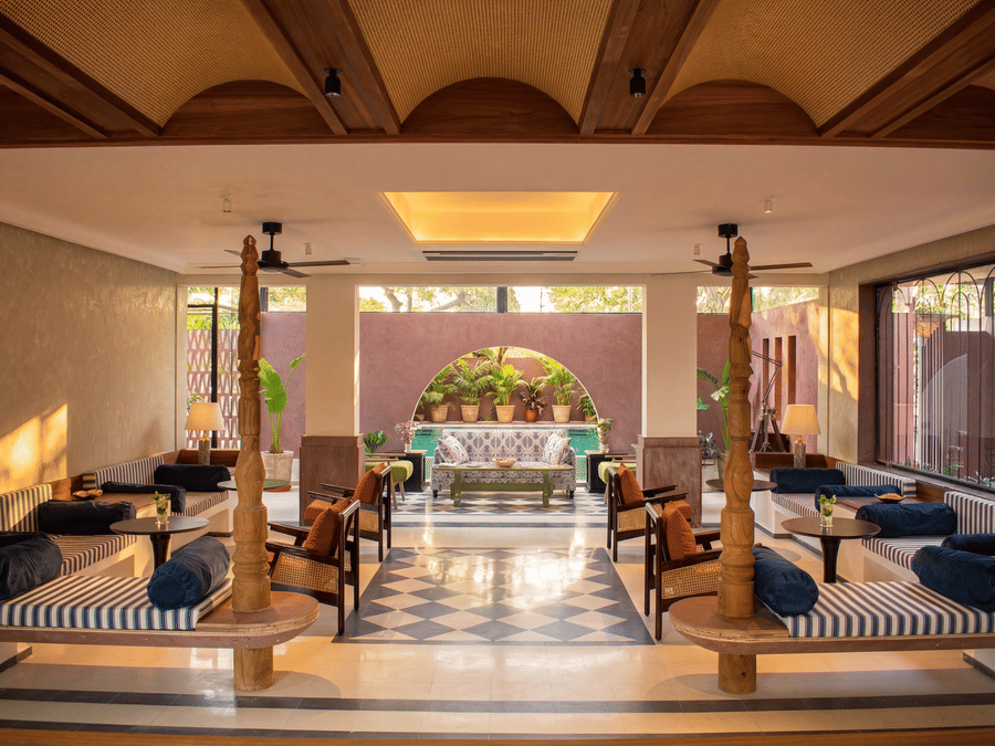 The indoor lounge seating area at The Sierra - By The Lake features wooden pillars, cushioned benches, low tables, and large windows overlooking the grounds.