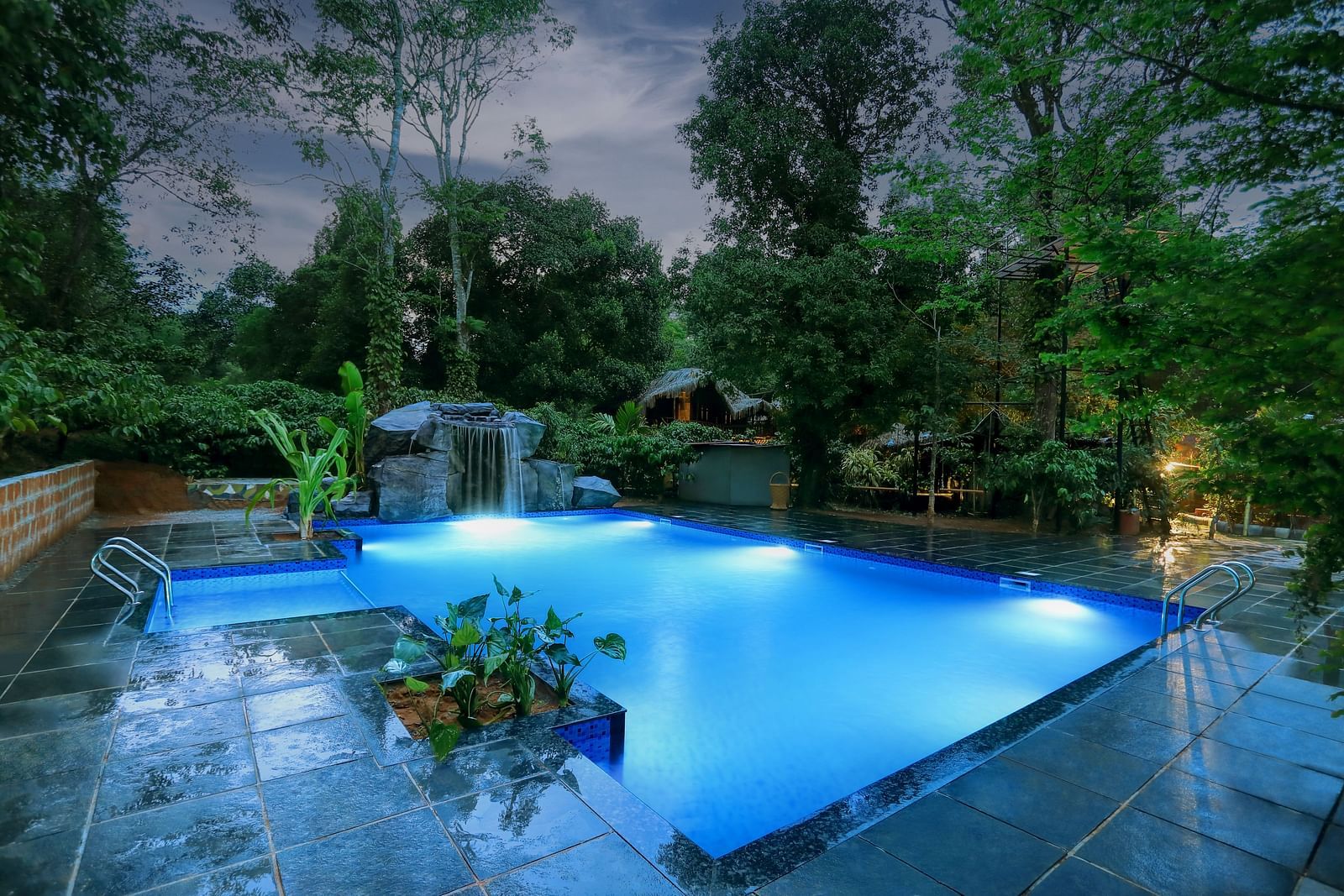 Illuminated resort pool at night with a waterfall and surrounding lush foliage - Evergreen County