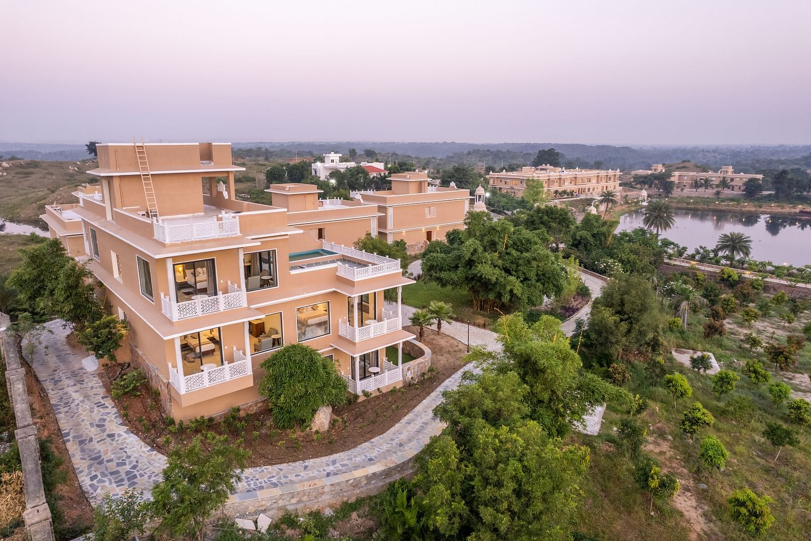 An image of our wellness retreat covered in lush green trees and a sky painted by the hue of the sun in the background - Rajbagh Wellness, Udaipur