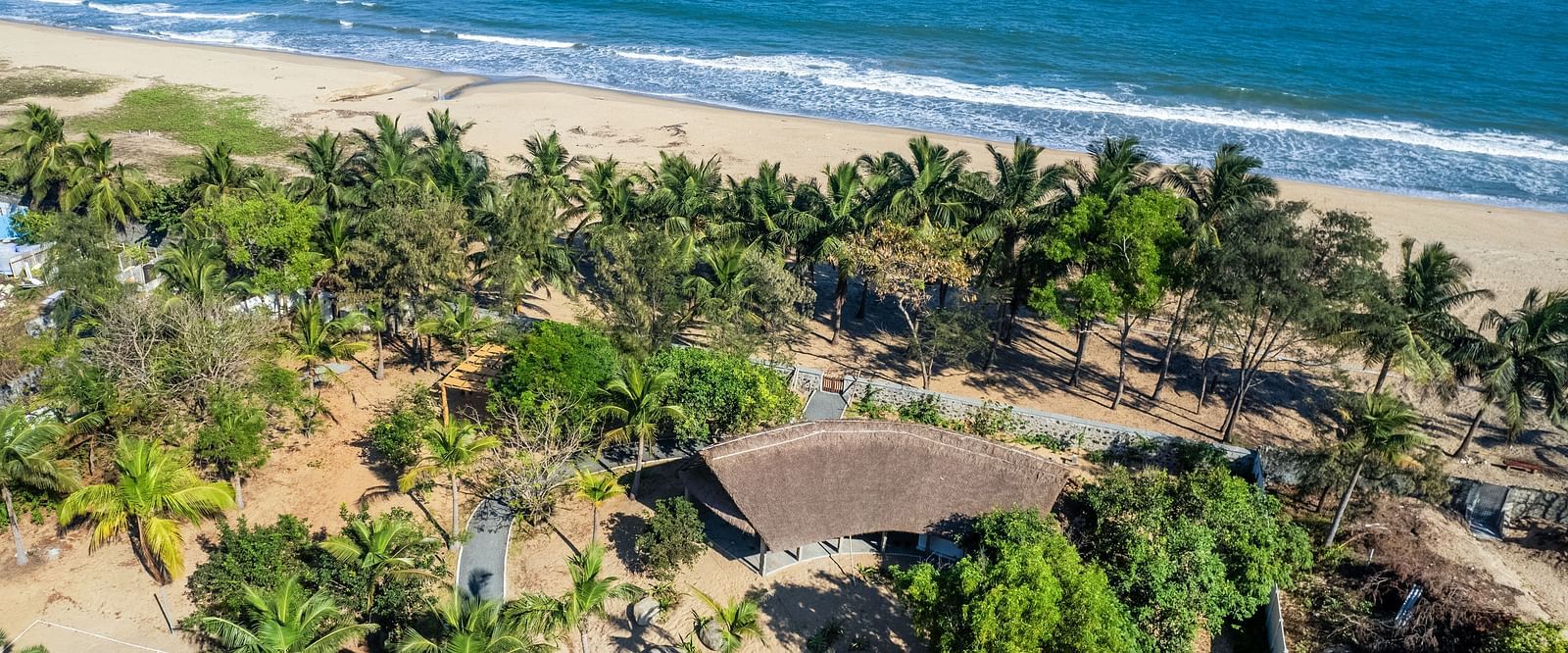 Aerial view of a tropical beach resort near Pondicherry with palm trees, buildings, and the ocean | Mango Hill Shallow Beach Resort ECR
