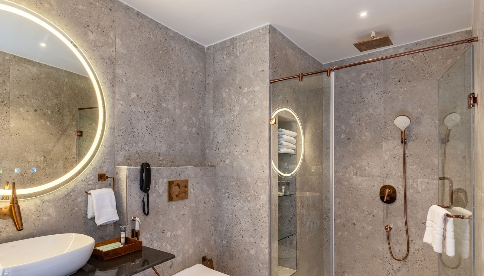 A modern bathroom at Osian Valley Resort & Spa with a stone basin on a dark counter, a large illuminated mirror, and a walk-in shower with a glass screen.
