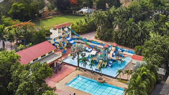 DGV Resort by Treat, Silvassa with a colourful waterpark featuring slides, splash areas, a swimming pool, and red-roofed buildings near a riverside