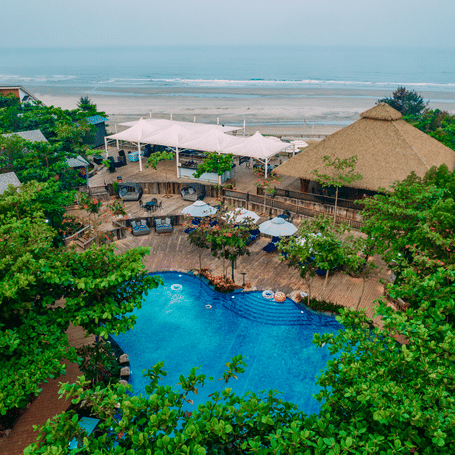 Tropical pool area at MAYFAIR On Sea, Morjim, Goa surrounded by dense palm trees and thatched-roof pavilions.