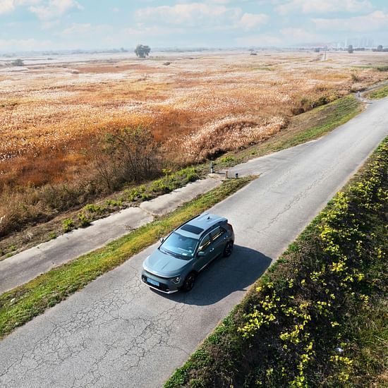 A far out view of a car driving in the middle of the road with greenery around