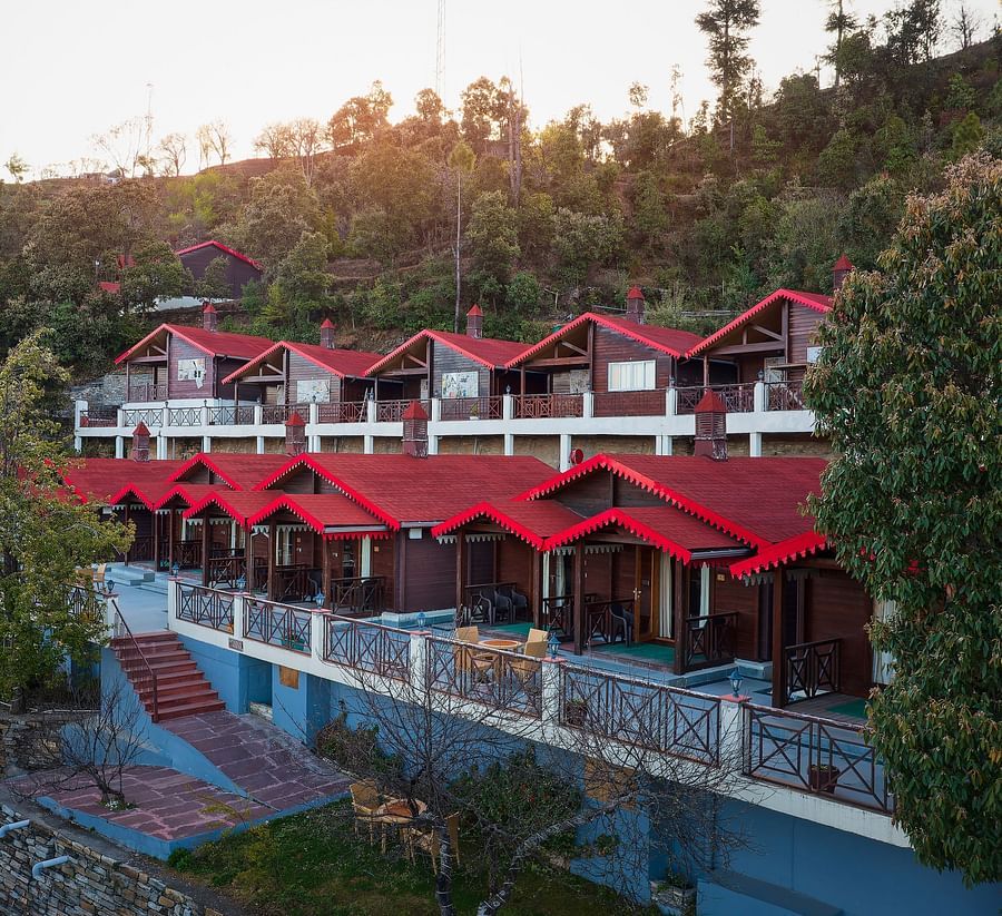 Buildings of  at Digantaa Resort in Mukteshwar with red roofs are located beside a swimming pool on a green hillside under a clear sky