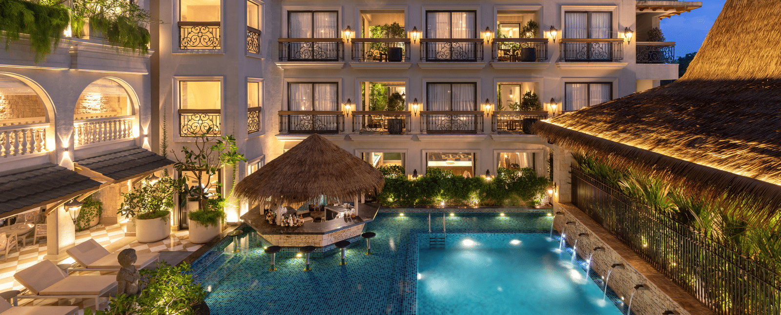 A beautiful swimming pool surrounding by the buildings of The Evren, Vagator, illuminated by exterior lighting during the evening.