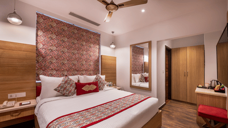 View of a Deluxe Room at Lords Inn Amritsar with a king bed, textured wall panel, wooden flooring, ceiling fan, and warm ambient lighting.
