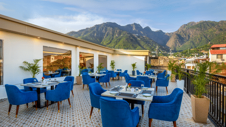 An outdoor rooftop dining terrace at Lords Inn Katra, one of the best hotels near Katra Vaishno Devi, offers tables, upholstered chairs, and a mountain view during daylight.