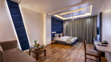 Elegant room at Lords Inn Sangam, Bhopal featuring a bed, blue accent wall, seating table with chairs, and rich wooden flooring.