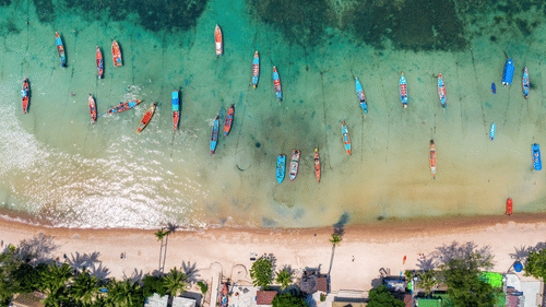 aerial view of long tail boats and a group of people on the beach