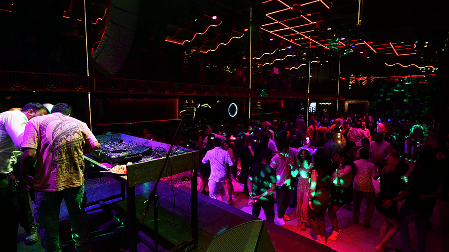 A DJ in a Hawaiian shirt spins tunes as the crowd dances beneath vibrant lights at Nysa Skybar, Bengaluru.