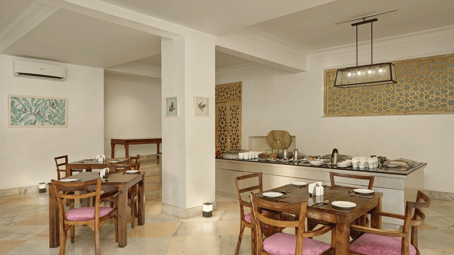 Lobby restaurant at Fateh Safari Resort, Kumbhalgarh featuring sets of tables and chairs and a kitchen counter where several utensils are kept.