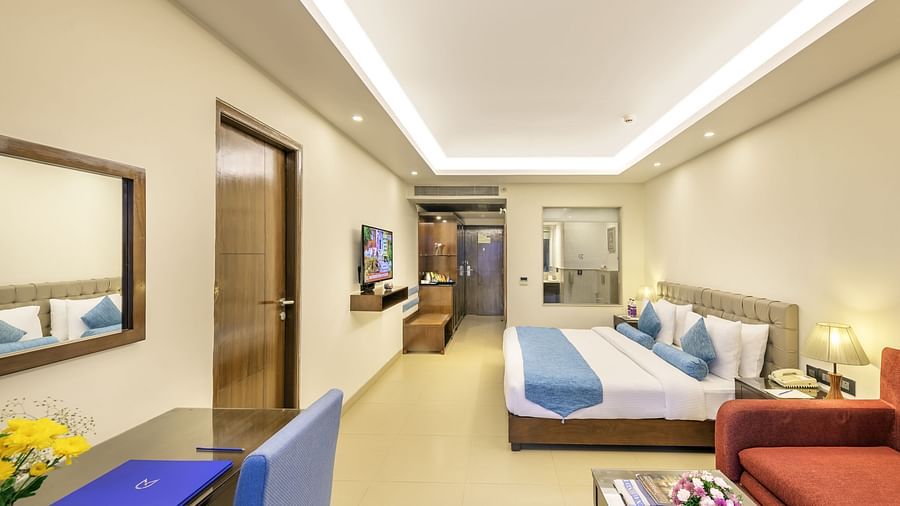 a wide angle view of a hotel room near candolim beach featuring a double bed, a work desk, an orange couch and coffee table and an attached washroom - Golden Tulip, Candolim, Goa