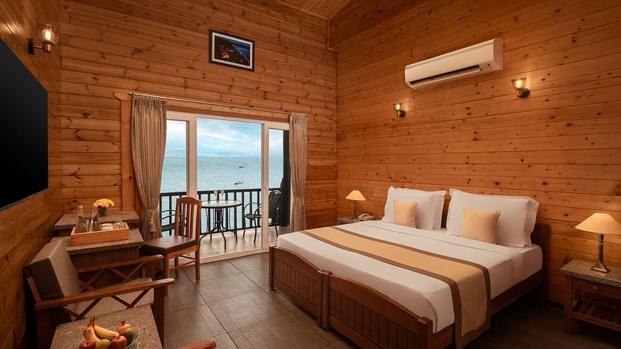 A wide angle shot of a room in Sindhudurg with a double bed, a seating area and a balcony - Highland Sarovar Portico, Sindhudurg