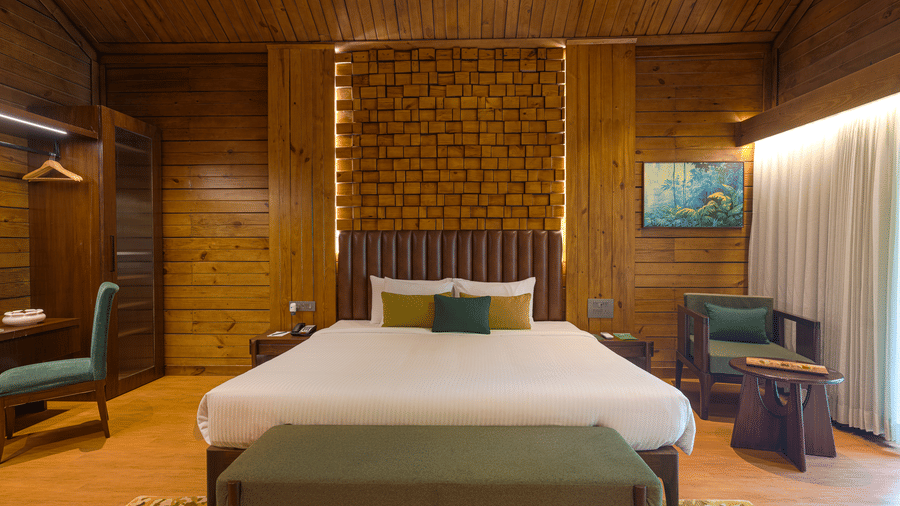 A room at The Ananta Udaipur, featuring a large bed, spreads, pillows, sofas, a wall art, and wooden wall.