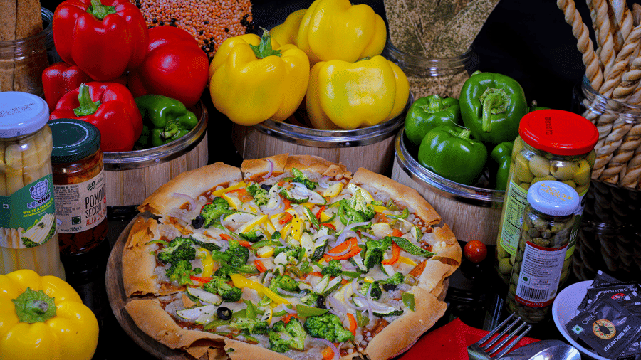 A pizza placed on a plate with capsicums in the backdrop at a dining space at Clarks Hotels.
